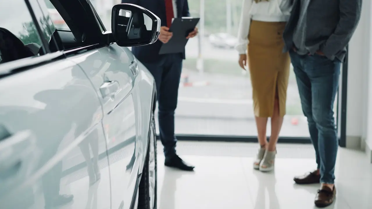 A dealer with a clipboard talking with two customers beside a car in a showroom
